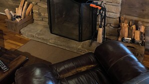 A stone fireplace with a black screen, a wooden bench, and a leather couch in a rustic room. - Authentic 1850’s Settlers cabin  High Speed Internet (Hendersonville)