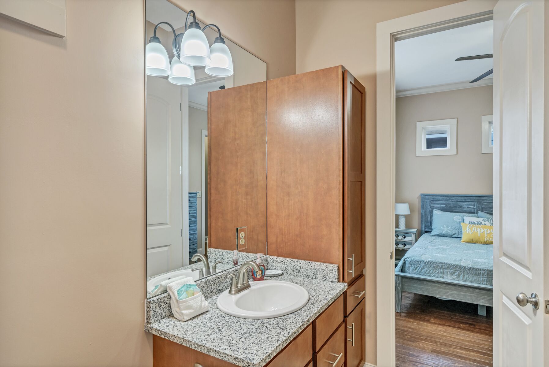 A bathroom with a granite countertop sink, wooden cabinets, and a mirror with three lights.