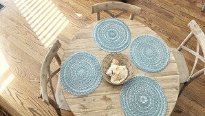 Una sala de estar con un sofá gris, un sillón azul, una mesa de centro de madera y una mesa de comedor con posavasos azules.