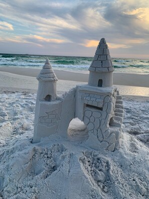A sandcastle with two towers and a small entrance, located on a beach with the ocean in the background.