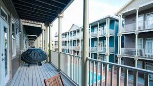 Un espacio exterior techado con una parrilla, una silla de madera y vistas a edificios de varios pisos con balcones.