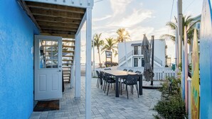 A patio area with a wooden table and chairs, a white door, and a view of palm trees and a building in the background. - Low Rider - Bottom Unit -  (Bradenton Beach)