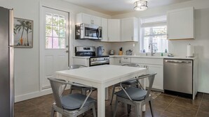 A modern kitchen with white cabinets, stainless steel appliances, and a dining area with four chairs. - Low Rider - Bottom Unit -  (Bradenton Beach)