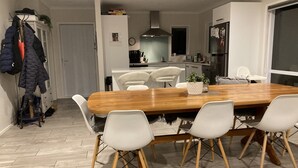 A modern kitchen with white cabinets, a wooden dining table, and white chairs. - Beach House (Tauranga)