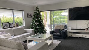 A modern living room with a large TV, a Christmas tree, and a sofa. - Beach House (Tauranga)