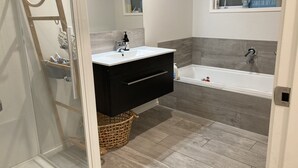 A modern bathroom with a white sink, black vanity, and a bathtub. - Beach House (Tauranga)