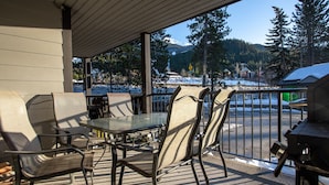 An outdoor patio with metal chairs and a glass table, overlooking a snowy landscape and a mountain in the distance.