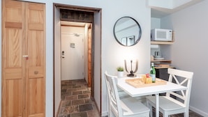 A room with a wooden door, a white table with chairs, a mirror, and a microwave on a shelf.
