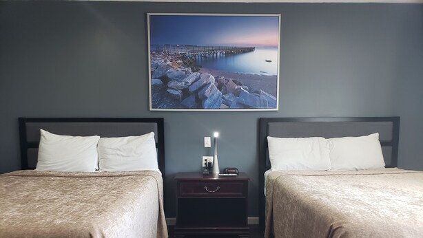 Habitación de hotel con dos camas, una mesita de noche con lámpara y un cuadro de un muelle en la pared.