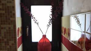Un bagno con parete piastrellata, una finestra e un vaso rosso con rami.