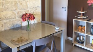 Zona pranzo con parete in pietra, orologio, vaso con fiori e mensola con oggetti decorativi.