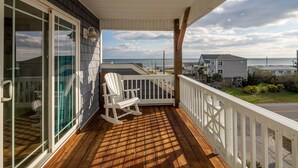 A wooden deck with a white railing, a rocking chair, and a view of the ocean and beach houses. - Gorgeous Ocean and Sound Views Await at Good Better Beach! (North Topsail Beach)