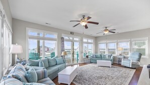 A spacious living room with a large window, a ceiling fan, a sofa set, and a view of the outside. - Gorgeous Ocean and Sound Views Await at Good Better Beach! (North Topsail Beach)