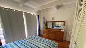 A bedroom with a striped bedspread, wooden dresser, and a mirror above it. - Tyrone Foreshore Treetop Cottage (Rye)
