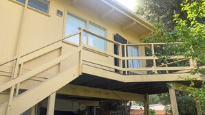 A two-story house with a covered porch and a staircase leading to a balcony. - Tyrone Foreshore Treetop Cottage (Rye)