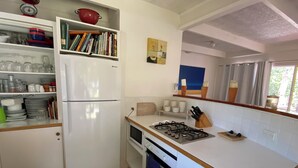 A compact kitchen with a refrigerator, stove, and shelves with kitchenware. - Tyrone Foreshore Treetop Cottage (Rye)