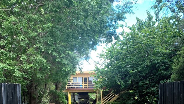 A pathway leading to a building with a covered area and a boat underneath. - Tyrone Foreshore Treetop Cottage (Rye)