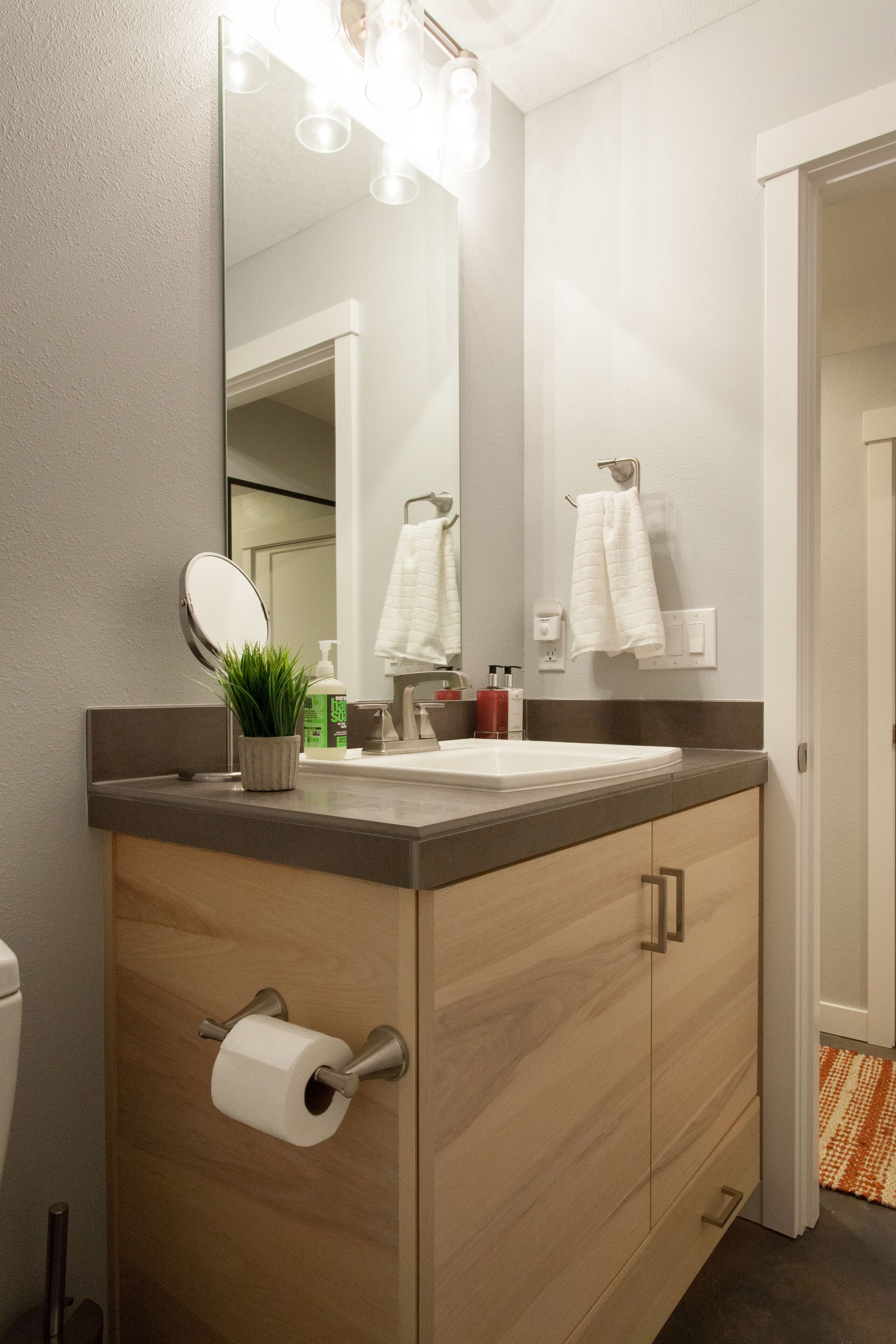 Une salle de bain moderne avec un meuble-lavabo en bois, un grand miroir et un porte-rouleau de papier toilette.