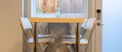 Un comedor con una mesa y cuatro sillas, una ventana con persianas y una puerta con cerradura.