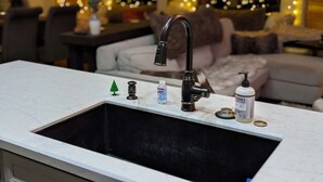 A kitchen with a black faucet, a small green Christmas tree, and a honey dispenser on the counter.