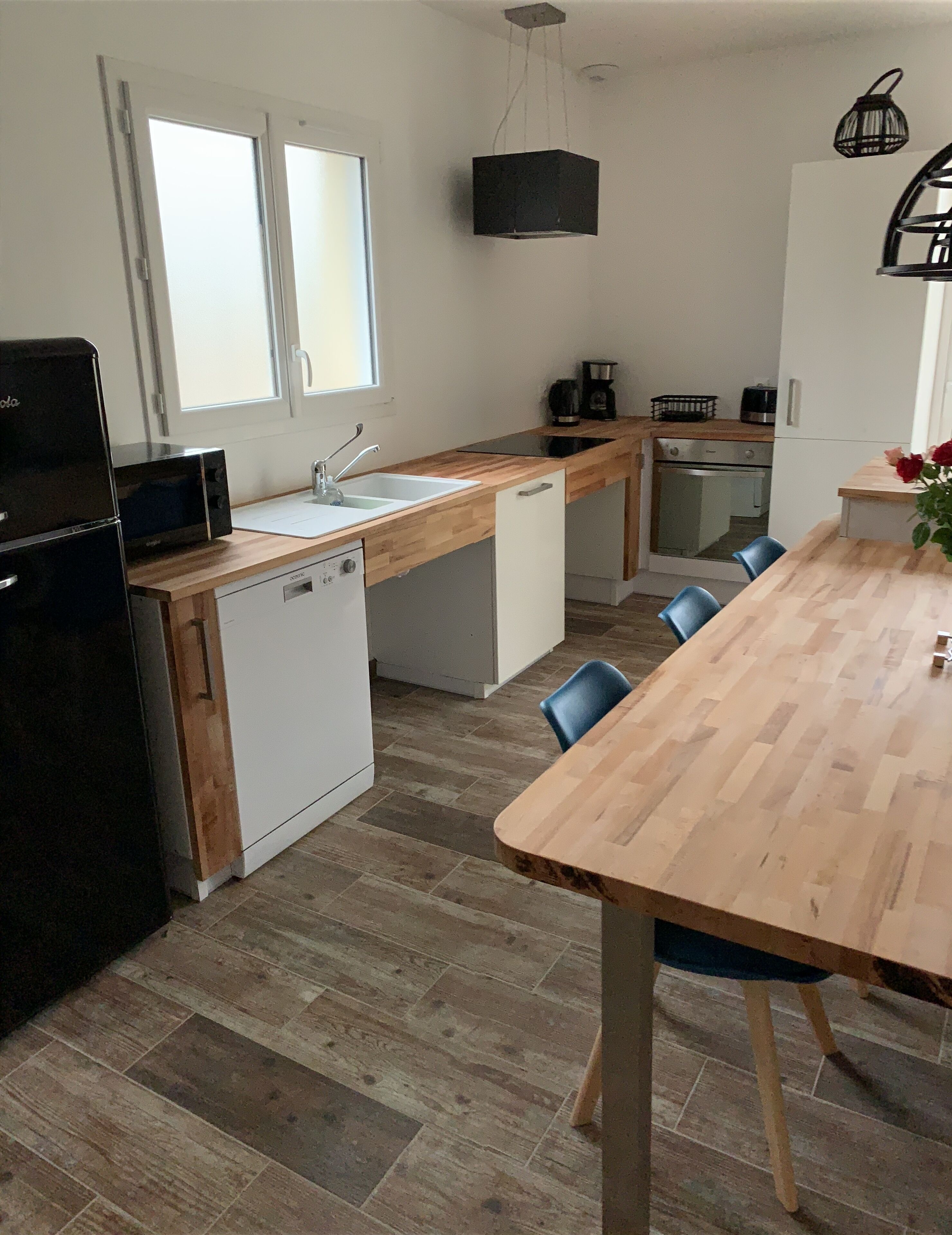 Une cuisine moderne dotée d’un plan de travail en bois, d’un évier, d’un réfrigérateur et d ’un coin repas avec des chaises.