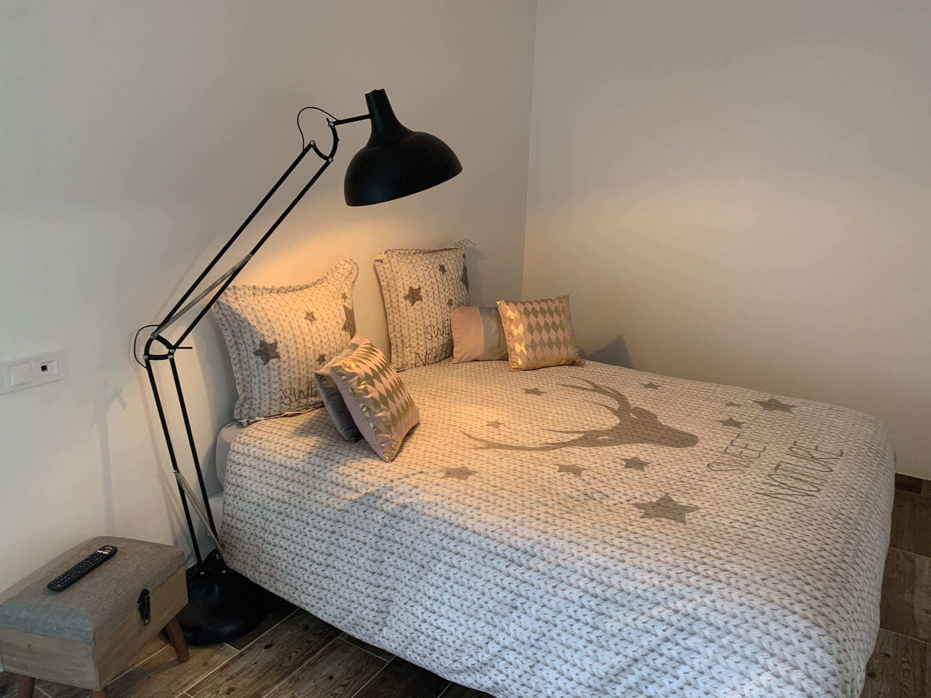 Ein ordentlich bezogenes Bett mit einer Decke mit Sternenmuster, eine schwarze Stehlampe und ein kleiner Nachttisch mit einer Fernbedienung.