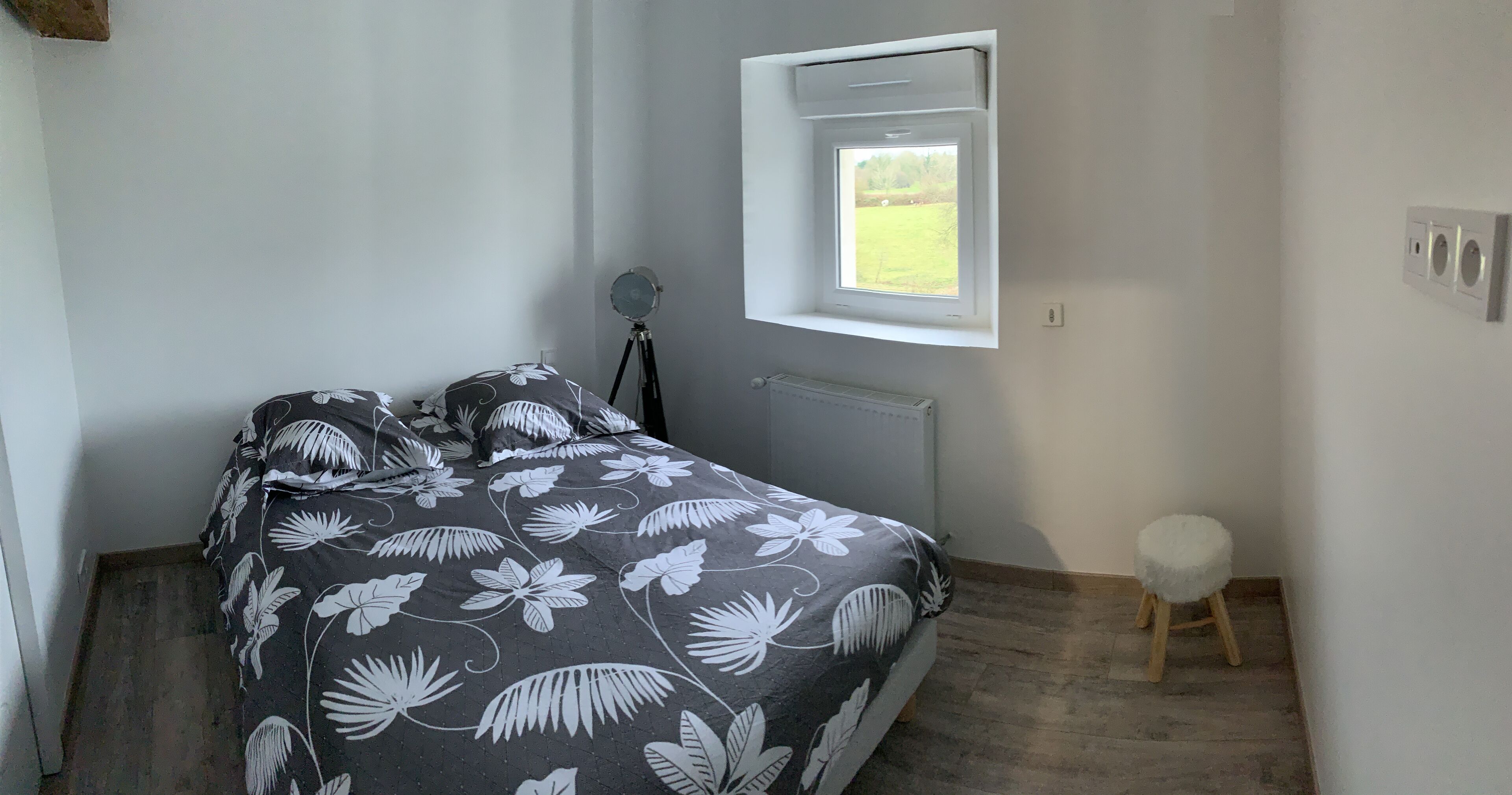 A bedroom with a bed, a small stool, a window, and a radiator.