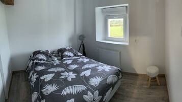 A bedroom with a bed, a small stool, a window, and a radiator.