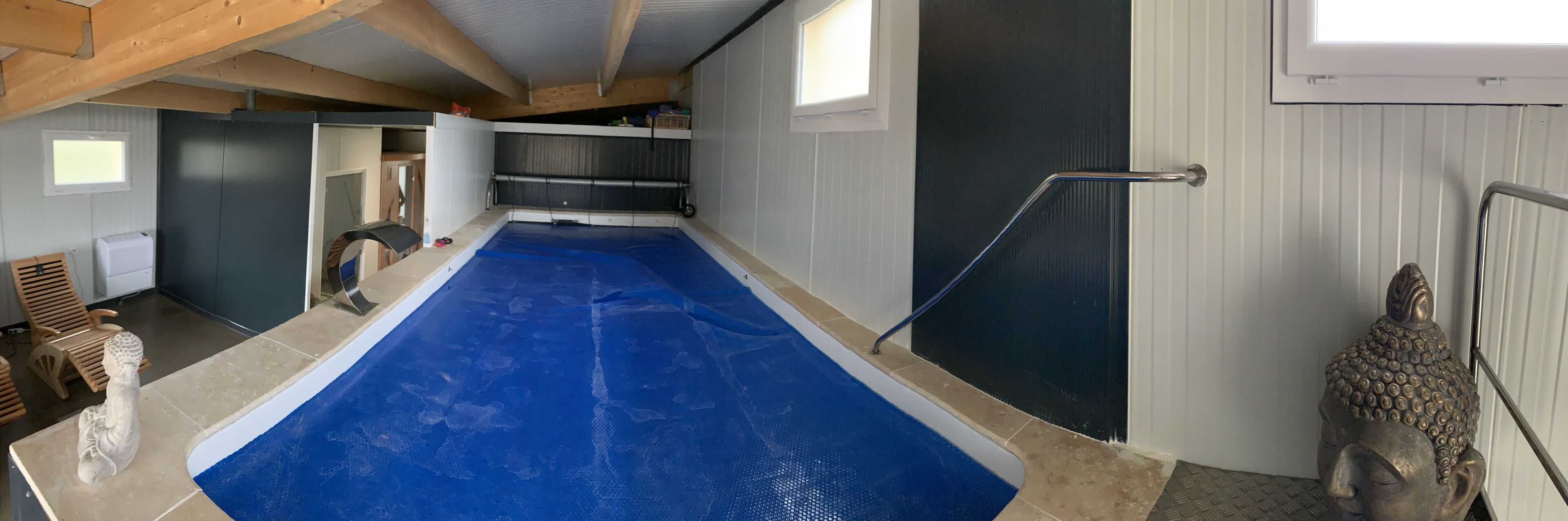 A swimming pool with a blue floor, wooden ceiling beams, and a Buddha statue.