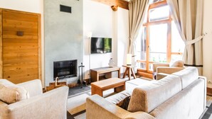 A living room with a sofa, TV, fireplace, and large windows.