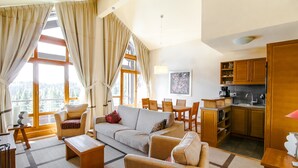 A spacious living area with a sofa, chairs, a coffee table, a dining table, and a kitchen area with wooden cabinets and a sink.