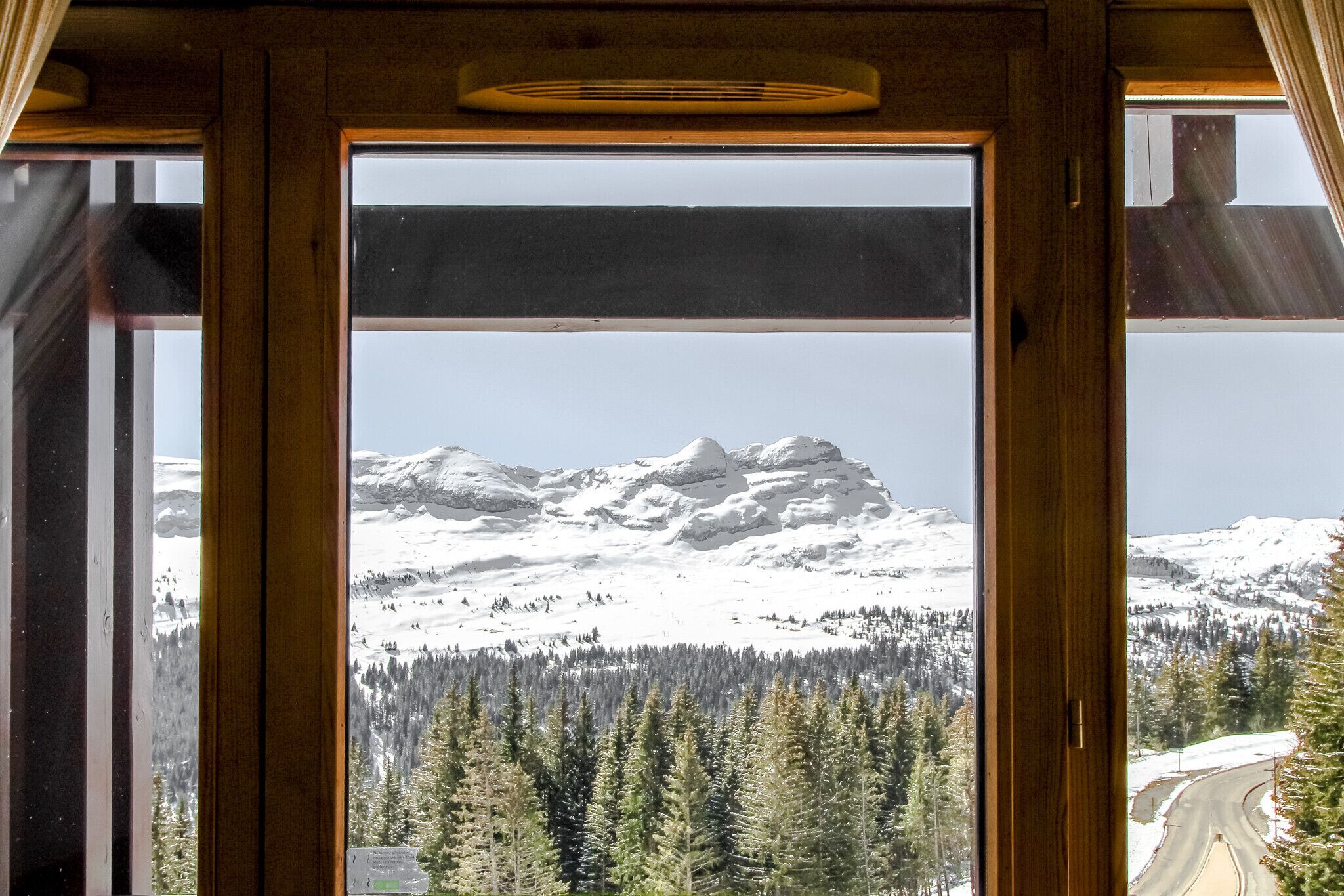 A view through a window of snow-covered mountains, a forest, and a road.