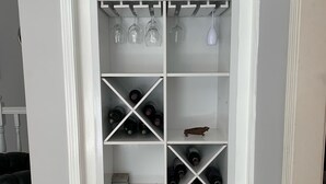 Una credenza per vino bianca con ripiani multipli, alcuni contenenti bottiglie e altri bicchieri da vino.