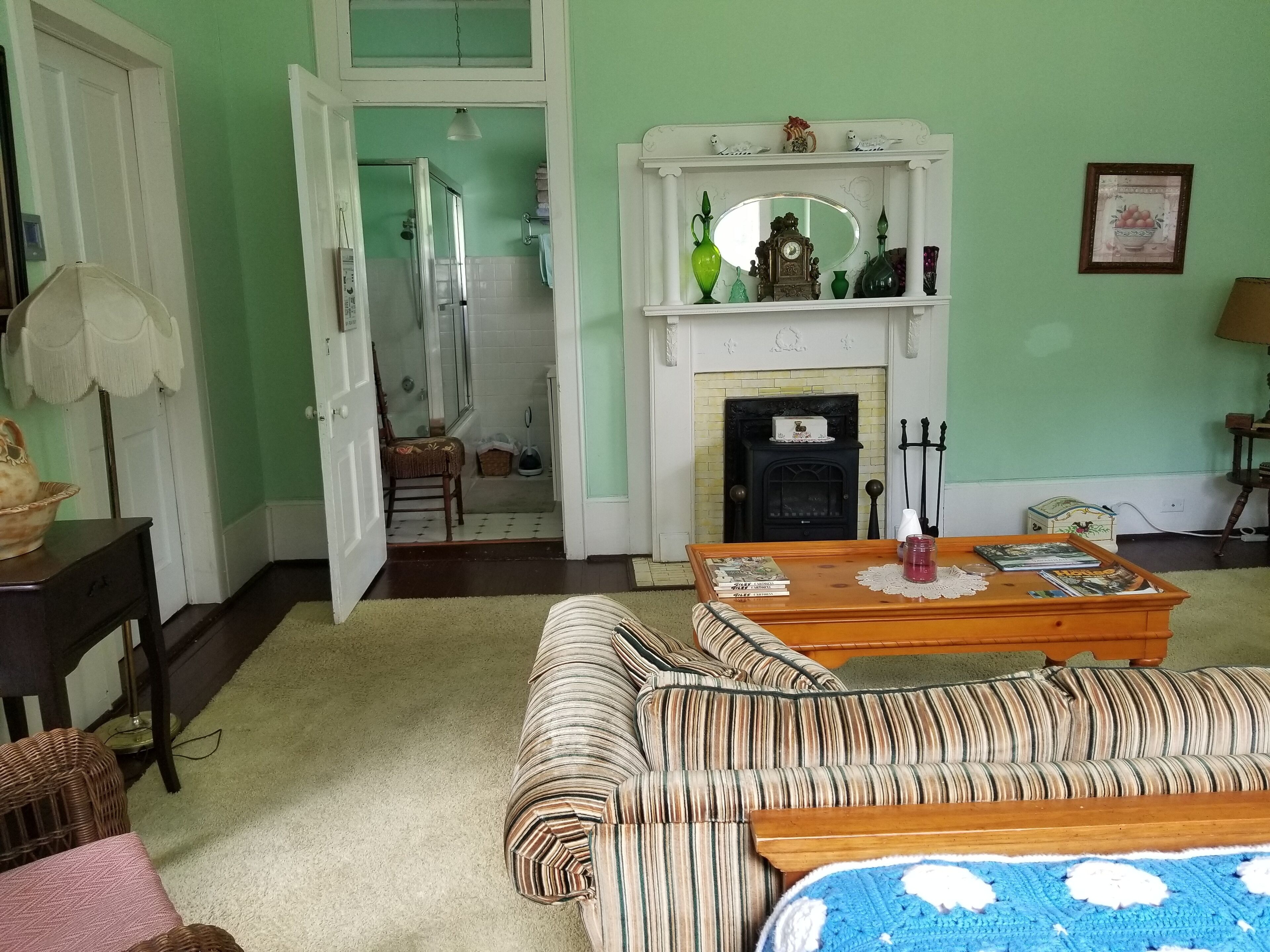 A living room with a fireplace, a sofa, a coffee table, and a door leading to a bathroom.