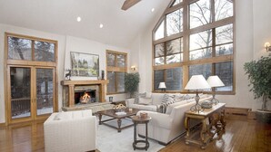A spacious living room with a fireplace, large windows, and a high ceiling.
