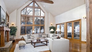A spacious living room with a high ceiling, large windows, and a cozy fireplace.