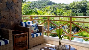 A balcony with wicker furniture, a stone wall, and a view of a lush landscape.