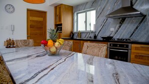 A kitchen with marble countertops, wooden cabinets, and a central island with fruit.