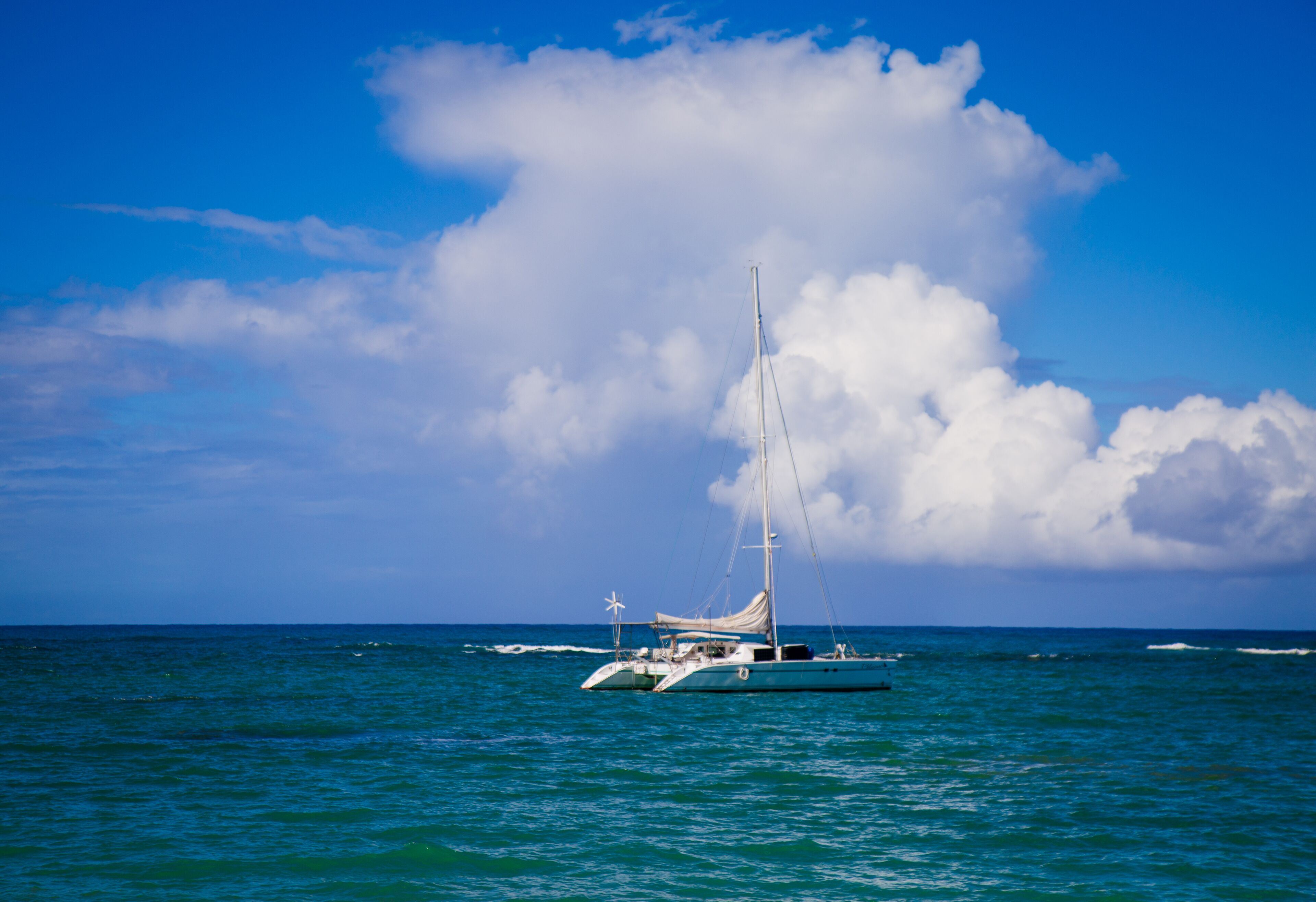 A sailboat on the ocean with a clear sky and clouds in the background.