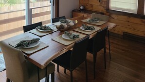 Ein Essbereich mit einem Holztisch, gedeckt für sechs Personen, einer hängenden Laterne und Blick durch große Fenster nach draußen.