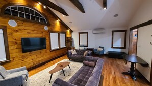 Ein gemütliches Wohnzimmer mit Holzwänden, einem großen Ecksofa, einem kleinen Couchtisch und einem an der Wand befestigten Fernseher.