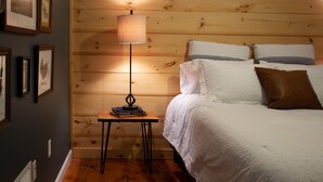 Et hyggeligt soveværelse med en trævæg, et sengebord med bøger, en lampe og en seng med puder.