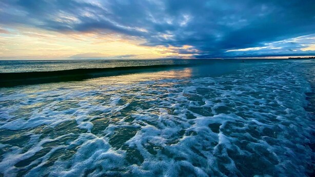 Una playa con olas y cielo nublado.
