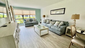 Un salón espacioso con un sofá gris, una mesa de centro de cristal y un aparador de madera.