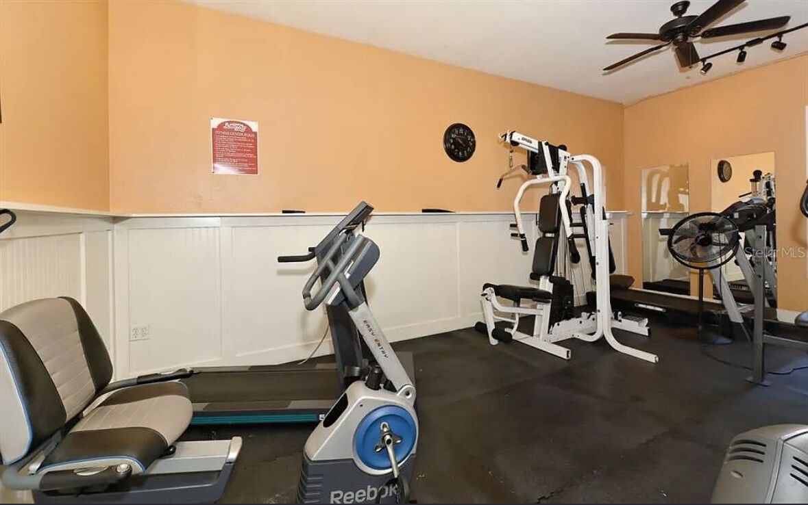 Un gimnasio con equipo de ejercicio, cinta de correr y ventilador de techo.