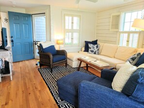 A living room with a blue door, a wicker chair, a beige sofa, and a patterned rug.