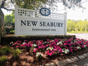 A sign for New Seabury Popponsett Inn with a decorative fence and vibrant flower beds.