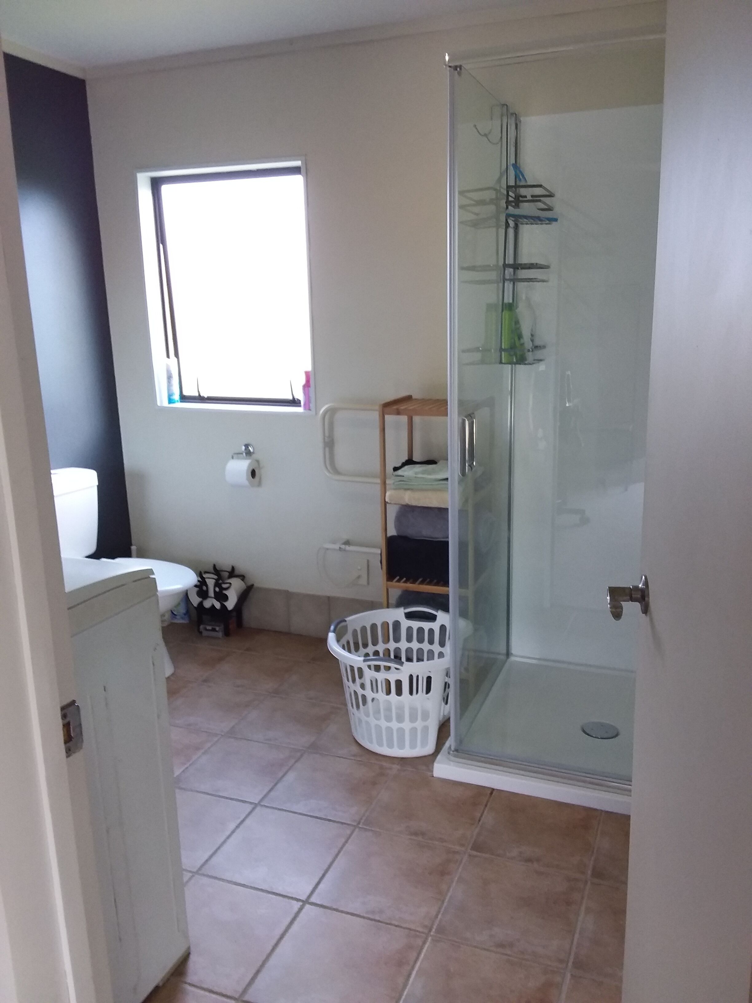 Ein Badezimmer mit Toilette, Fenster, Dusche und Wäschekorb.