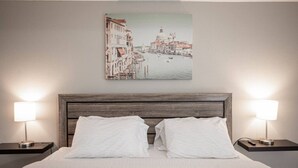 Ett hotellrum med en säng, två sängbord, en sänggavel och en tavla som föreställer en stadsbild, upphängd på väggen.