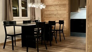 A dining area with a wooden wall, a chandelier, and a view into the kitchen. - Apartment Ariel by Interhome (Saanenmöser)